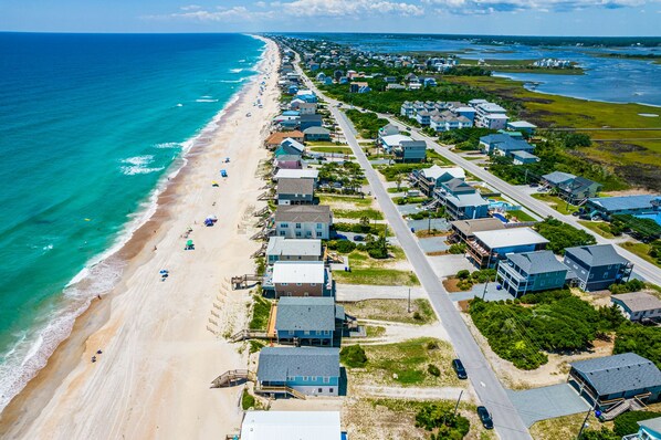 Vista aérea de una zona residencial costera con casas a lo largo de la playa, cielos despejados y mar en calma.