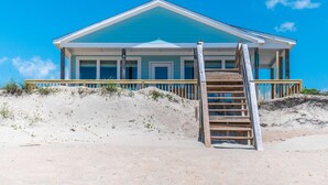 Una casa sulla spiaggia con una scala di legno che conduce a un portico.
