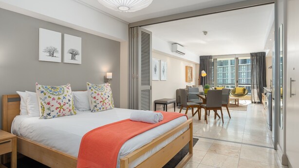 A modern hotel room with a large bed, a dining area, and a view of the city. - Spacious Studio Apartment on the Canals in CT (Cape Town)