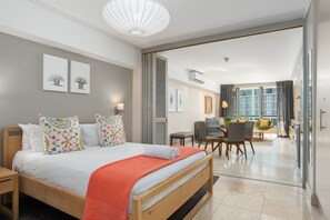 Una habitación de hotel moderna con una cama grande, un área de comedor y vistas a la ciudad.