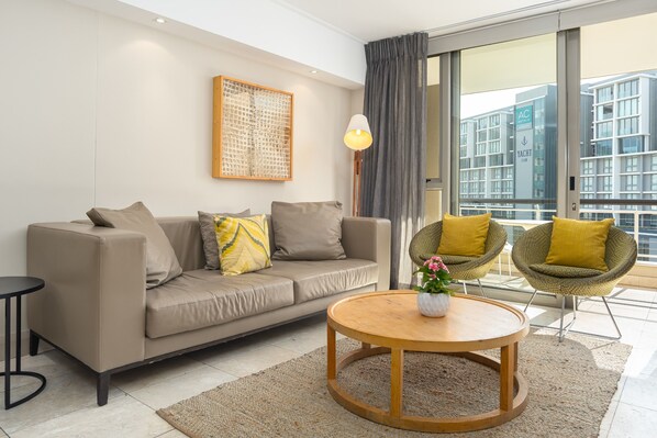 Una sala de estar moderna con un sofá, dos sillones, una mesa de centro y un ventanal con vistas a edificios.