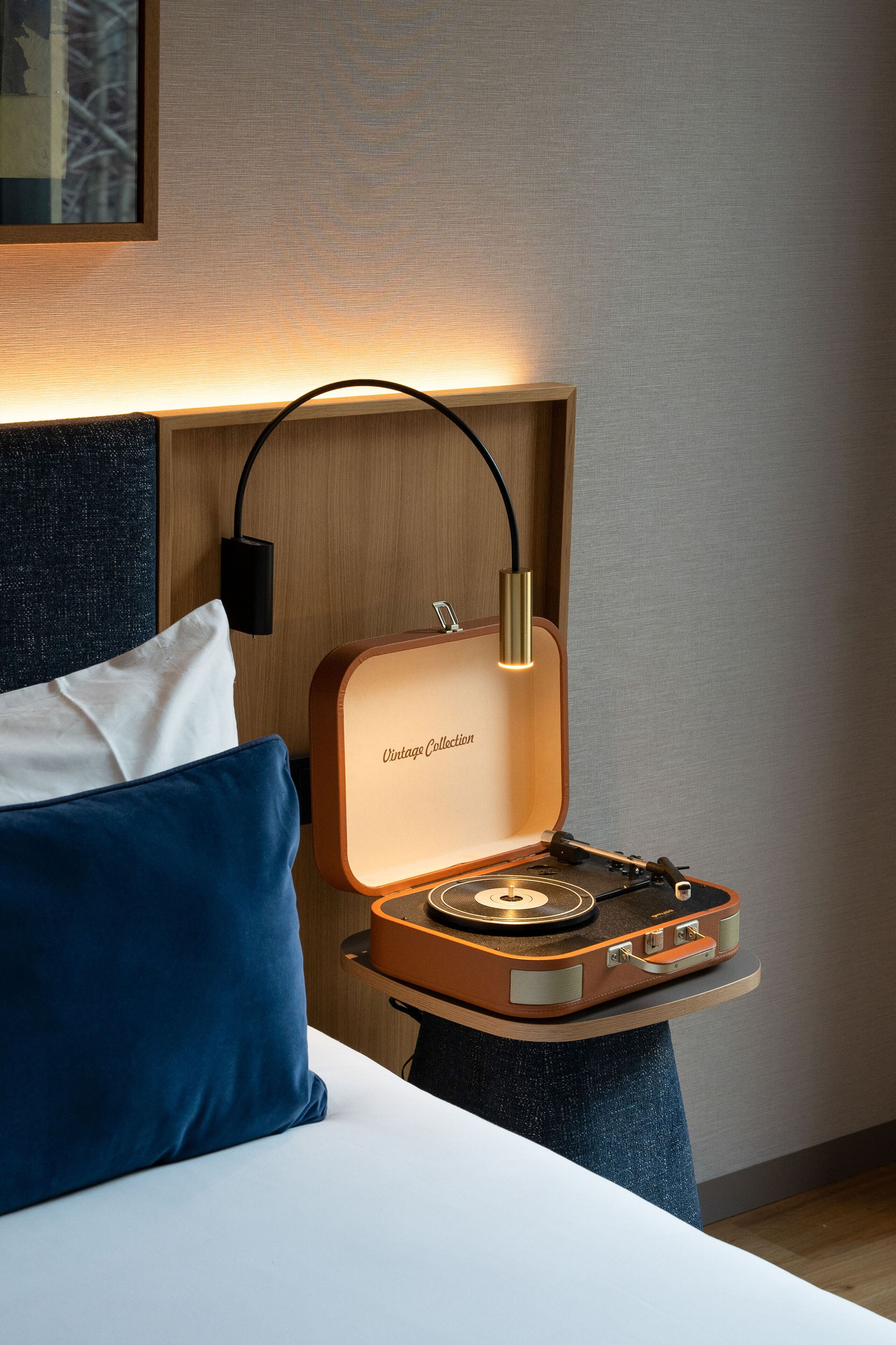 A bed with a white and blue pillow, a wooden headboard, and a vintage collection record player on a side table.