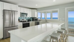 A modern kitchen with a large island, stainless steel appliances, and a view of the ocean.