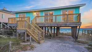 A beachfront property with a wooden deck and a staircase leading to a balcony.