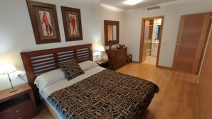 A bedroom with a large bed, a nightstand, a dresser, a mirror, and a door leading to a bathroom. - NON STRESS Arena Beachfront (Alboraya)