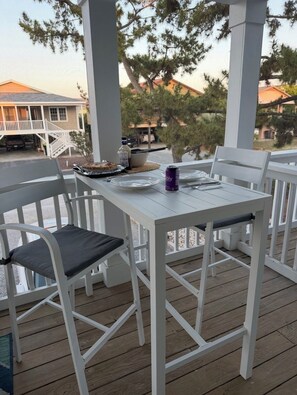 A covered outdoor deck with white furniture, a table set for dining, and a view of a house and trees in the background. - Bucket List Beach Retreat, Sunset Beach - with EV Charger
HGTV WINNER! (Sunset Beach)
