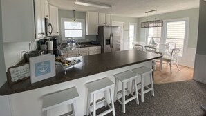 Une cuisine spacieuse avec des meubles blancs, un grand îlot central doté de tabourets, un réfrigérateur et un coin repas avec des chaises.