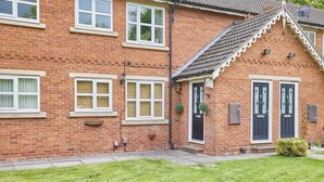 A brick house with a front porch, two doors, and a small garden with a lawn and a few plants. - The Garden Flat (Darlington)