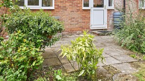 A brick house with a white door and windows, a concrete pathway, and various green plants. - The Garden Flat (Darlington)