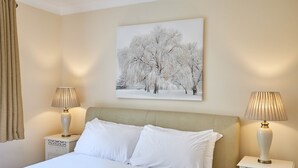 A neatly made bed with white linens, two bedside tables with lamps, and a painting of trees on the wall. - The Garden Flat (Darlington)