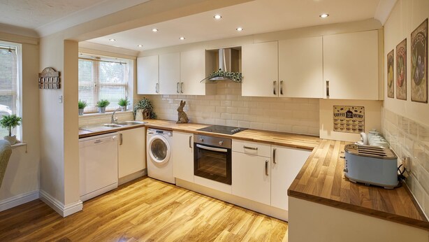 A modern kitchen with wooden flooring, built-in appliances, and a window with potted plants. - The Garden Flat (Darlington)