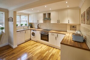 A modern kitchen with wooden flooring, built-in appliances, and a window with potted plants. - The Garden Flat (Darlington)