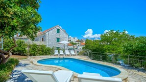 A swimming pool with white lounge chairs, a stone building with a red roof, and lush greenery in the background. - Villa Bonaca - Three Bedroom Villa, Sleeps 6 (Sumartin)