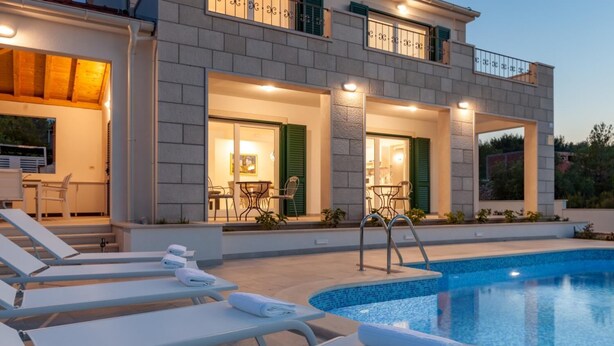 Une maison moderne à deux étages, dotée d’une piscine, d’un espace extérieur aménagé et d’un patio bien éclairé.