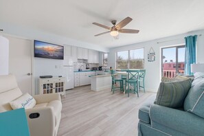 A modern kitchen with white cabinets, a dining area with teal chairs, and a ceiling fan. - Modern Beauty by the Beach Gulf View Balcony &Pool (St. Pete Beach)