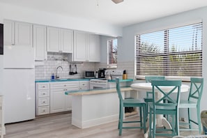 Una cucina moderna con mobili bianchi, un piano di lavoro blu e un'area pranzo con sedie color acquamarina.