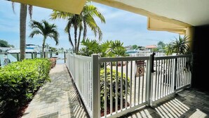 A gated outdoor area with a paved walkway, palm trees, and a view of a marina with boats.
