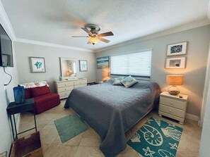 A bedroom with a bed, a dresser, a nightstand, a ceiling fan, and a window with blinds.
