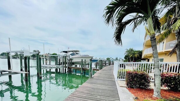 A wooden dock extending into calm water, with a building and palm trees on the right.