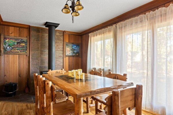 Een houten eetkamer met een grote tafel en stoelen, een zwarte schoorsteen en kunstwerken aan de muur.