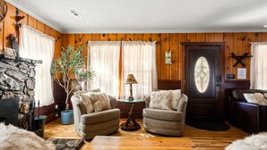 A cozy living room with wooden walls, a stone fireplace, two armchairs, a coffee table, and a potted plant. - A rustic retreat nestled in the heart of Boulder Bay (Big Bear Lake)