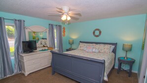 A bedroom with a bed, dresser, TV, and ceiling fan. - Seaside Escape in Pebble Beach  (Emerald Isle)