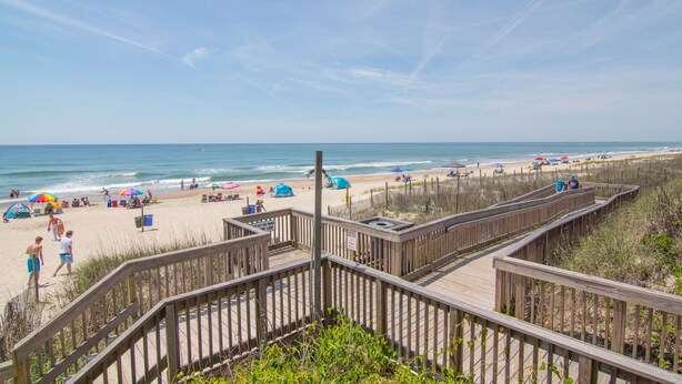 A beach with wooden boardwalks, umbrellas, and beachgoers. - Seaside Escape in Pebble Beach  (Emerald Isle)