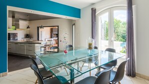Una cocina moderna con una mesa de comedor de vidrio, sillas y vista al patio trasero a través de amplios ventanales.