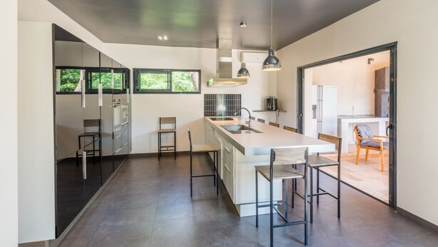 Una cocina moderna con una isla grande, taburetes de bar y vistas al exterior a través de las ventanas.