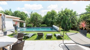 Un patio trasero con piscina, sillas de descanso y zona de comedor.