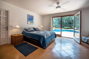 Un dormitorio con cama, ventilador de techo, ventana con vista a una piscina y una puerta.