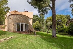 Una casa de piedra con un patio, rodeada de árboles y un césped bien cuidado.