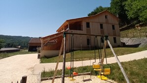 Un bâtiment rustique en bois, avec un chemin de terre menant à une balançoire, situé dans un cadre rural.