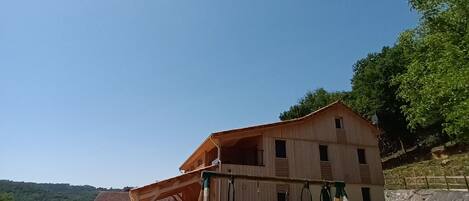 A rustic wooden building with a dirt path leading to a swing set in a rural setting.