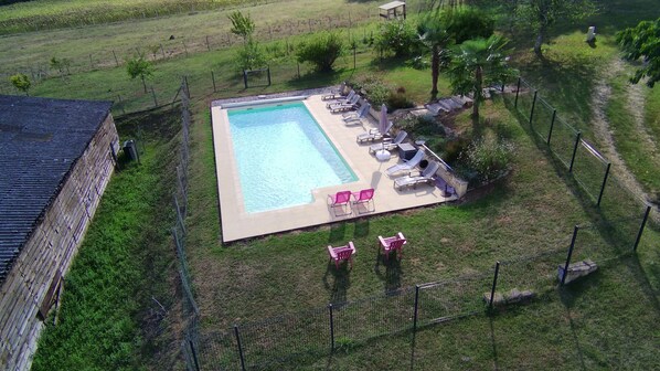 An aerial view of a swimming pool with lounge chairs and a fenced area.