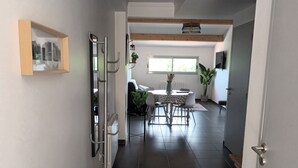 A hallway with a dining area, a coat rack, and a door leading to another room.