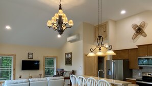 A spacious living area with a large sofa, a dining table with chairs, a kitchen with modern appliances, and a chandelier.