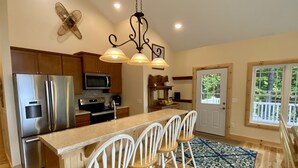 A modern kitchen with stainless steel appliances, a central island with bar stools, and a view of the outdoors through a large window.