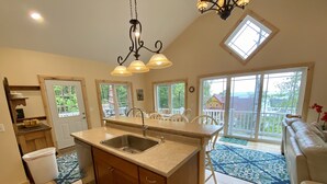 A spacious kitchen with a large island, a dining area with chairs, and a view of the outdoors through large windows.
