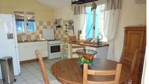 A compact kitchen with white cabinets, a stove, and a sink. There's a dining table with chairs and a fruit basket.