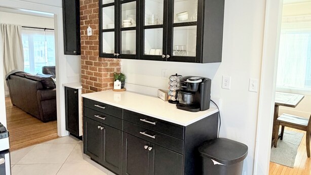 Cozinha moderna com armários pretos, parede de tijolos e uma máquina de café.
