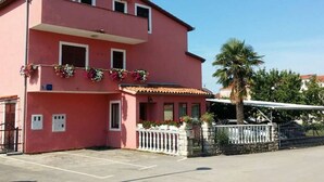 A pink building with a balcony, a gated entrance, and a parking area.