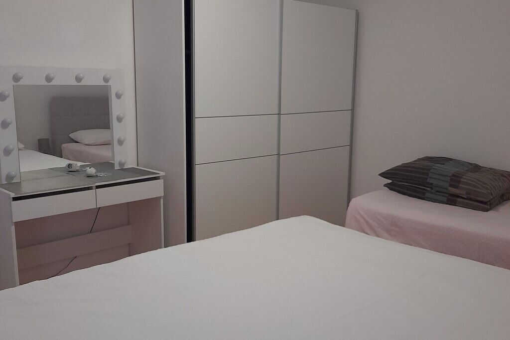 Un dormitorio con cama, mesita de noche, espejo iluminado y armario.