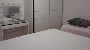 A bedroom with a bed, a bedside table, a mirror with lights, and a wardrobe.