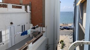 Un balcón con vistas al mar, un muro de ladrillo y un edificio blanco con contraventanas.
