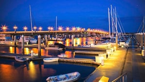 Un puerto deportivo al atardecer con barcos amarrados, un puente al fondo y senderos bien iluminados.