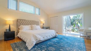 Un dormitorio con una cama grande, dos lámparas de noche, un tapete azul estampado y vistas a un patio con mobiliario exterior.