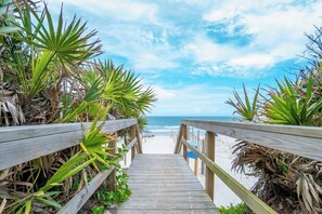 A wooden boardwalk leading to a beach with palm trees on either side.