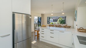 Eine moderne Küche mit weißen Schränken, einem Edelstahlkühlschrank, Holzstühlen und einem großen Fenster mit Blick nach außen.
