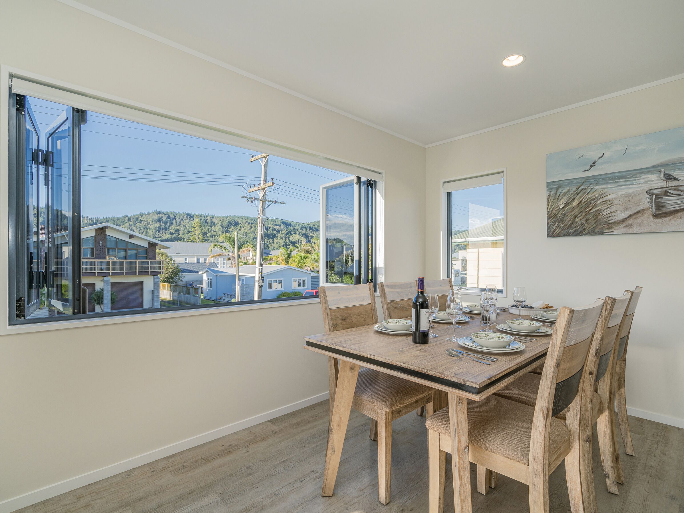 A dining area with a large window, a painting, and a table set for four.